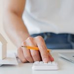 close up man hand counting on calculator with house&rsquo;s model on invoice letter to summary of refinance expense for planning and manage money about home loan mortgage and interest rates for people lifestyle concept